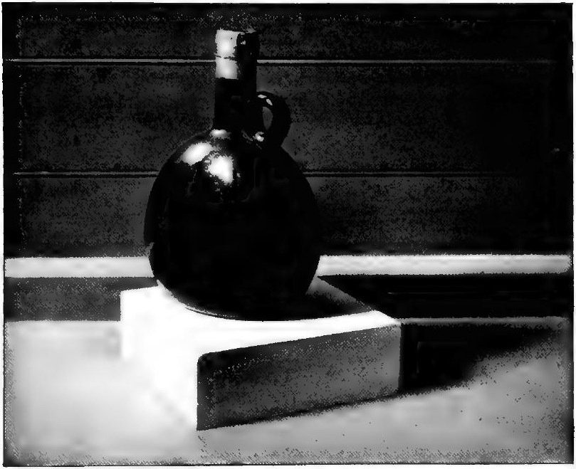 Cross's photograph of a black bottle with a handle, standing on a white block, with two small bright window reflections on its body.